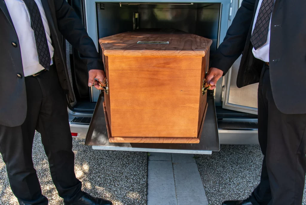 Porteurs funéraires chargeant un cercueil en bois dans le corbillard.