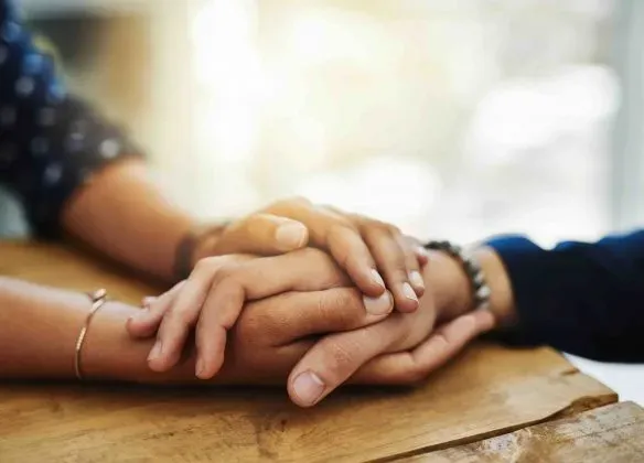 Deux personnes se tenant la main sur une table en bois en soutien.